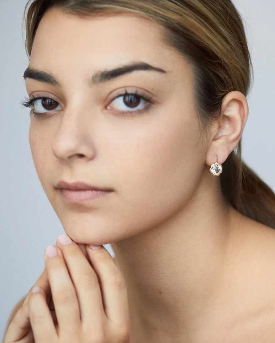 Three-quarter close-up of Blossom Drop earring with white topaz in 18K yellow gold worn by model against soft neutral background