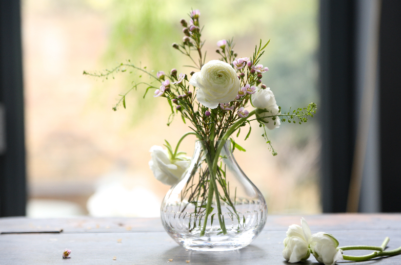 Angled view of small crystal vase with lens engraving showing rounded bulb shape and short stem holding white blooms on table