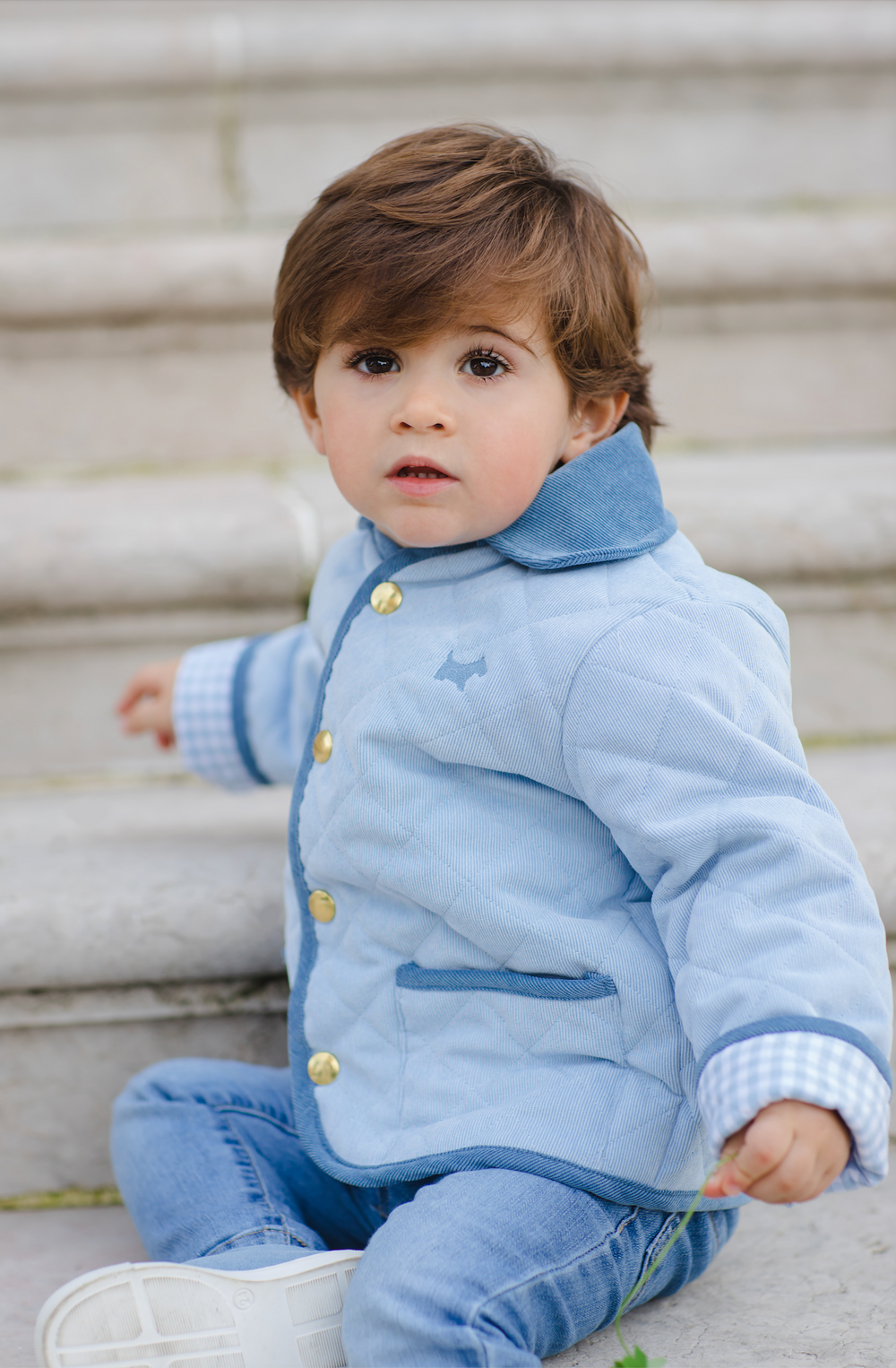Three-quarter view of classic blue quilted jacket on toddler showing gold snaps, gingham lining, and front pockets