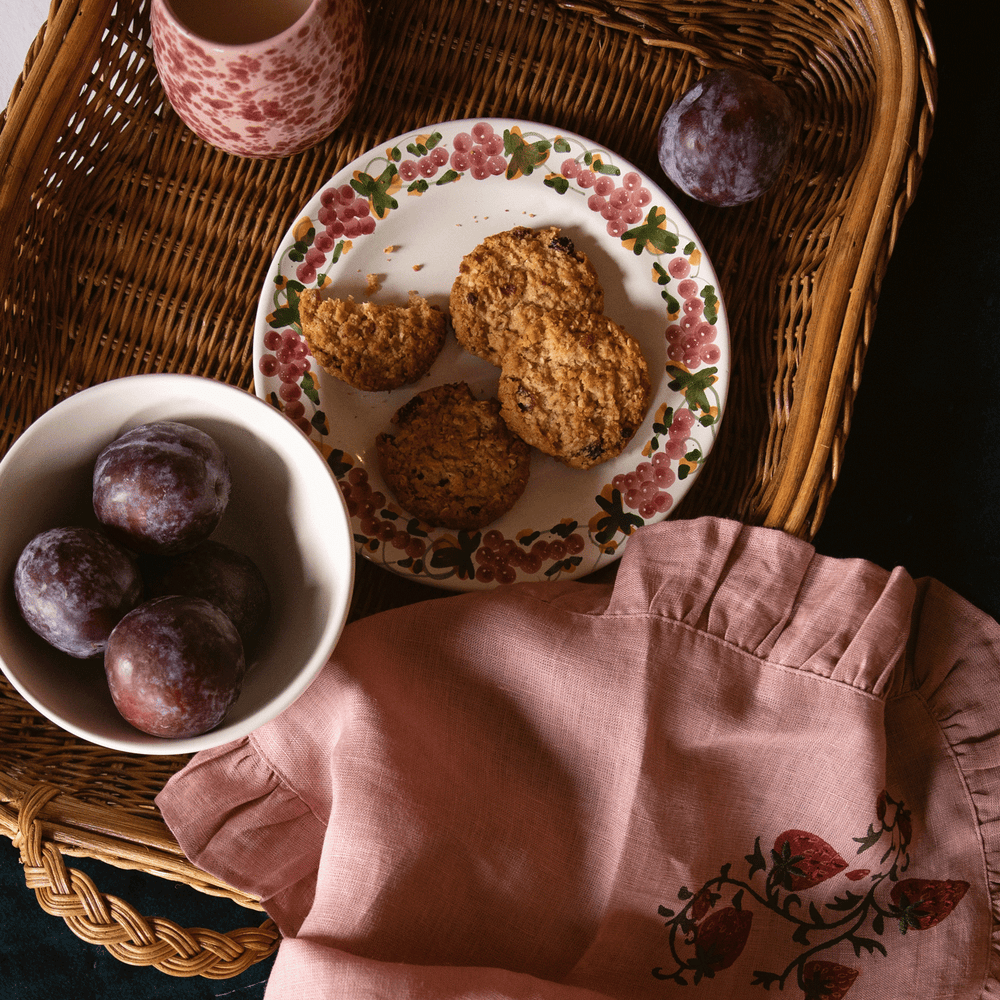 Top down view of Vine Dinner Plate showcasing hand-painted pink grapevine rim with cookies on a wicker tray