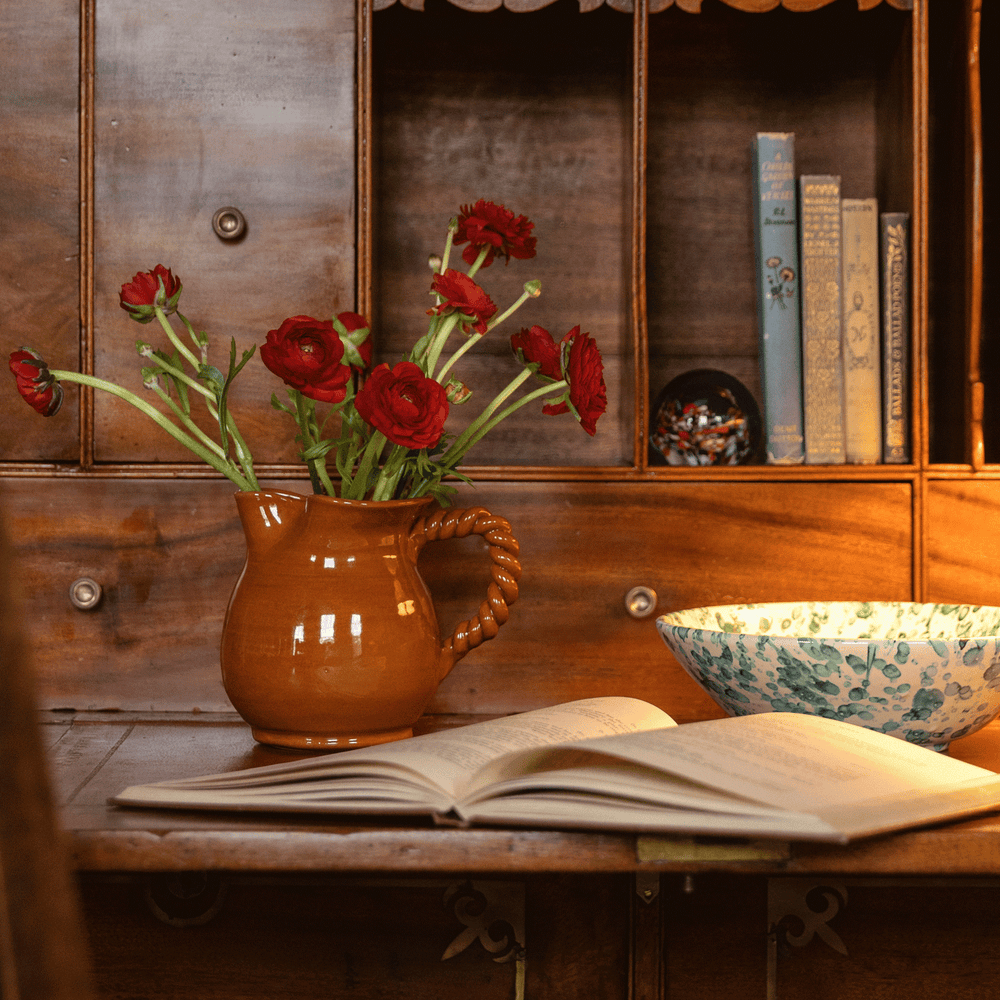 Front view of Louise Jug with twisted handle and glossy terracotta glaze on a wooden desk with an open book