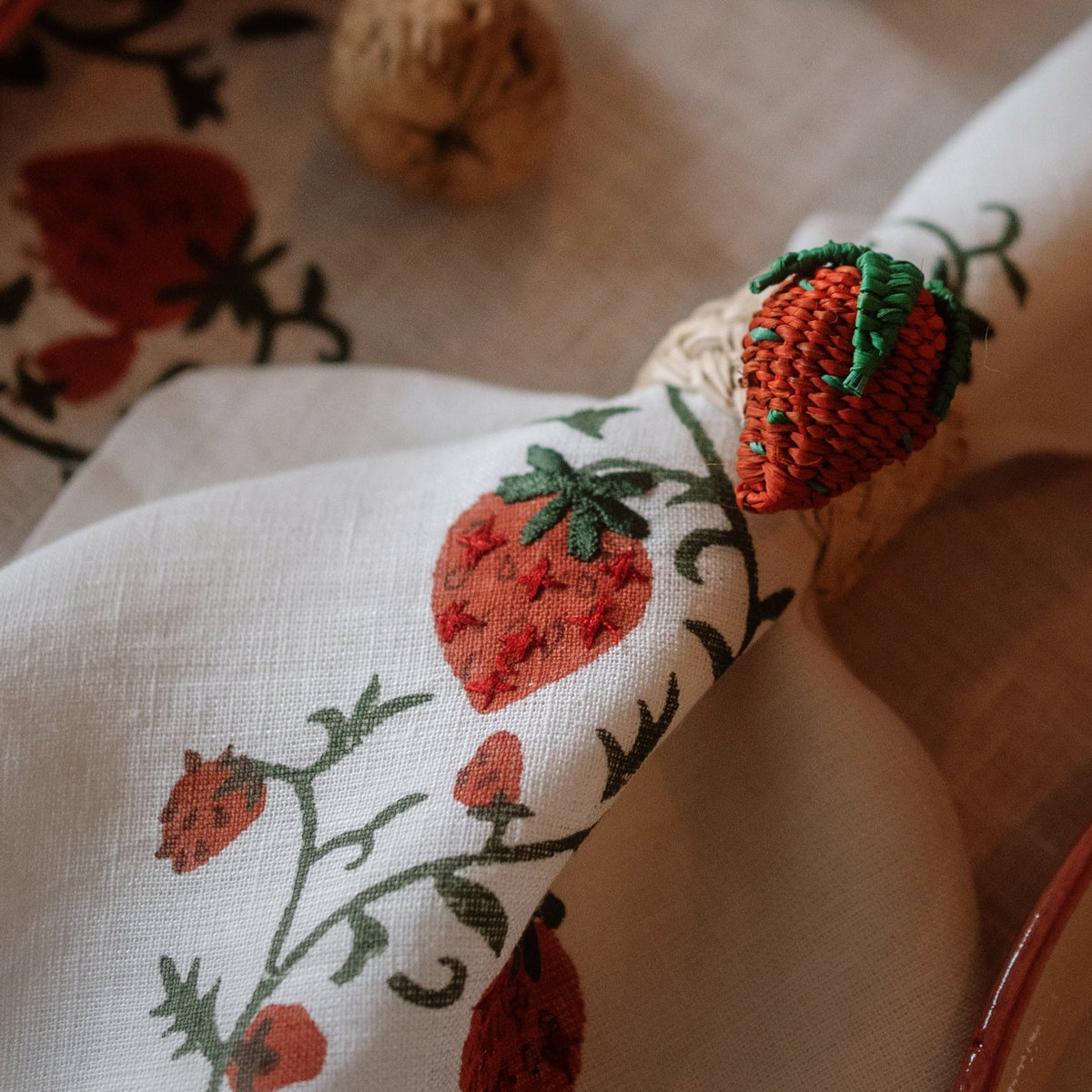 Close-up of Fraises des Bois napkin showcasing hand stitched strawberry embroidery and ruffled border on a tabletop
