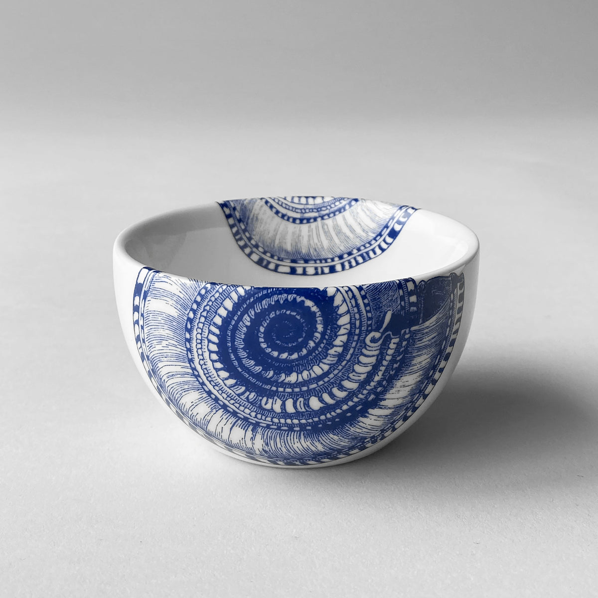 Close-up view of Shells Snack Bowl showcasing blue shell pattern on creamy porcelain with a gray background
