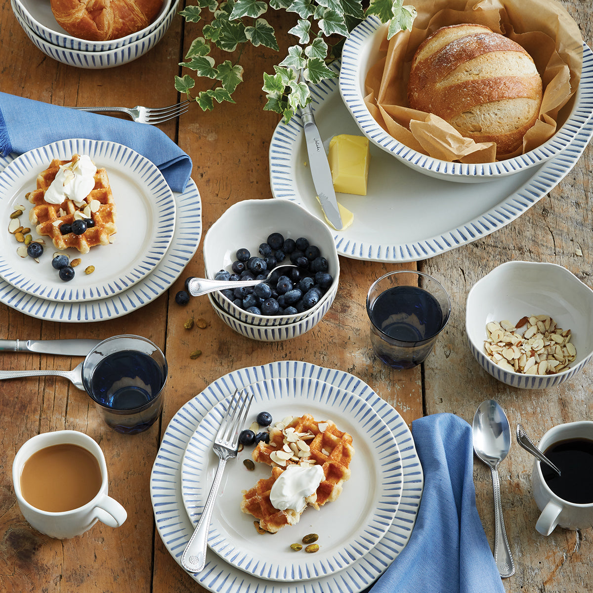 Breakfast table featuring a blue and white striped serving platter with bread, waffles, fruit, and coffee