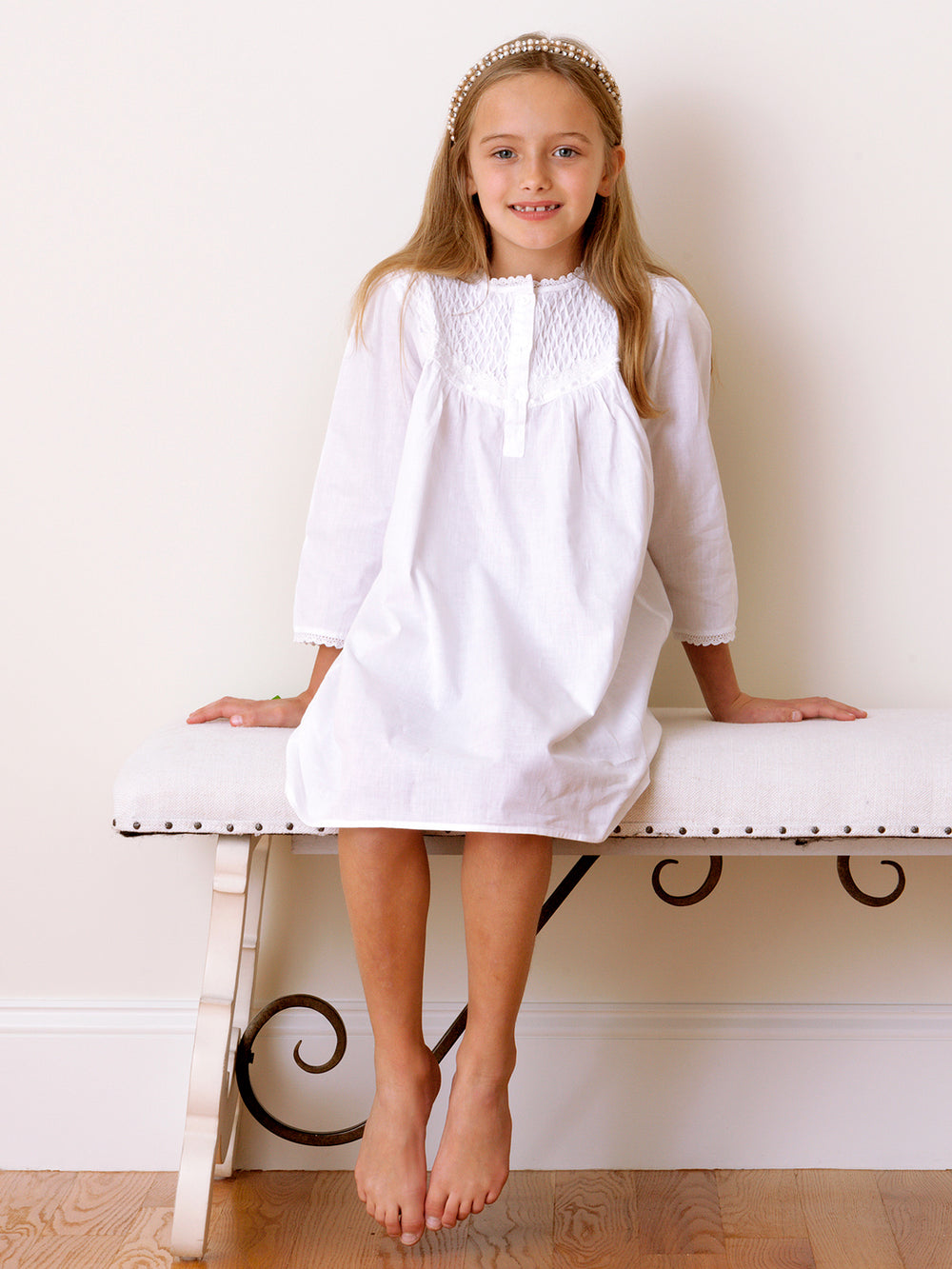 Front view of Sophia white cotton long-sleeve girls’ dress on a seated model showing smocked yoke and eyelet lace