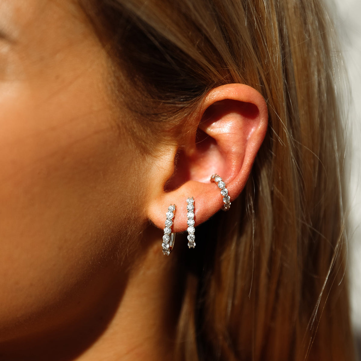 Close up of ear wearing Sparkler Cuff showing a row of round diamonds on a gold ear cuff with two matching diamond hoops