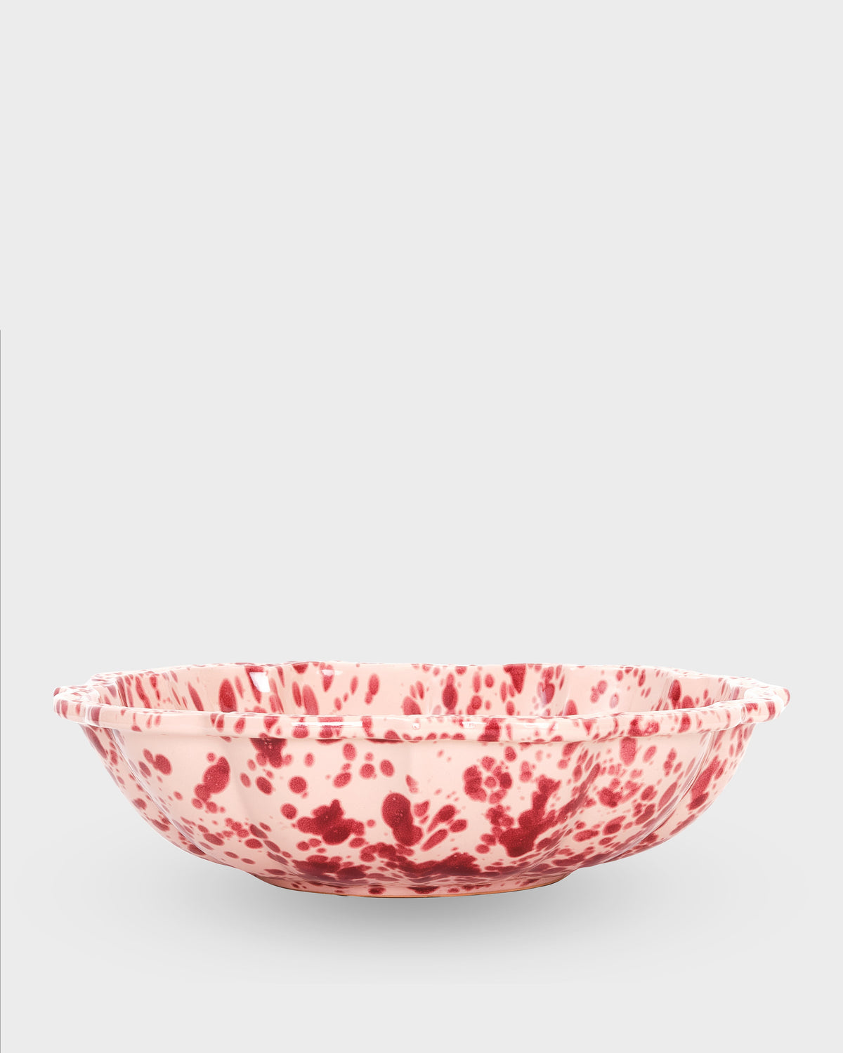 Angled view of Speckled Serving Bowl in Pink showcasing hand-painted speckles with a light gray background