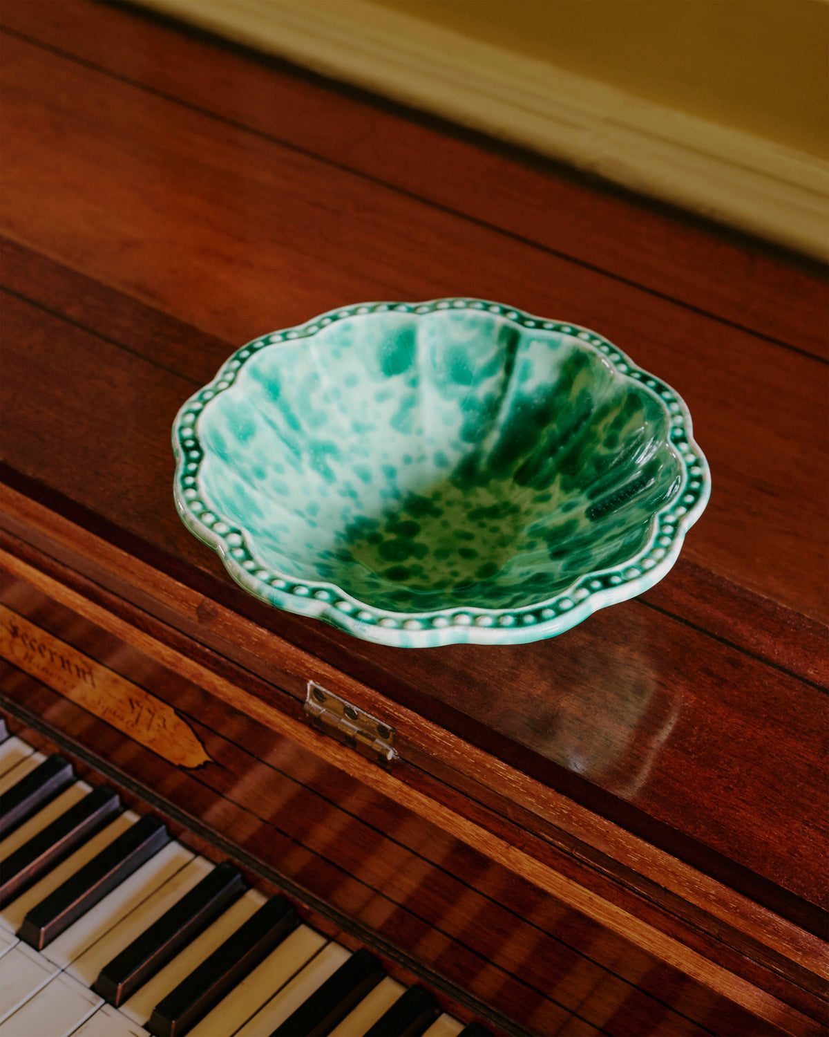 Close-up view of Speckled Small Bowl in Green showcasing hand-painted speckled ceramic on a wooden piano