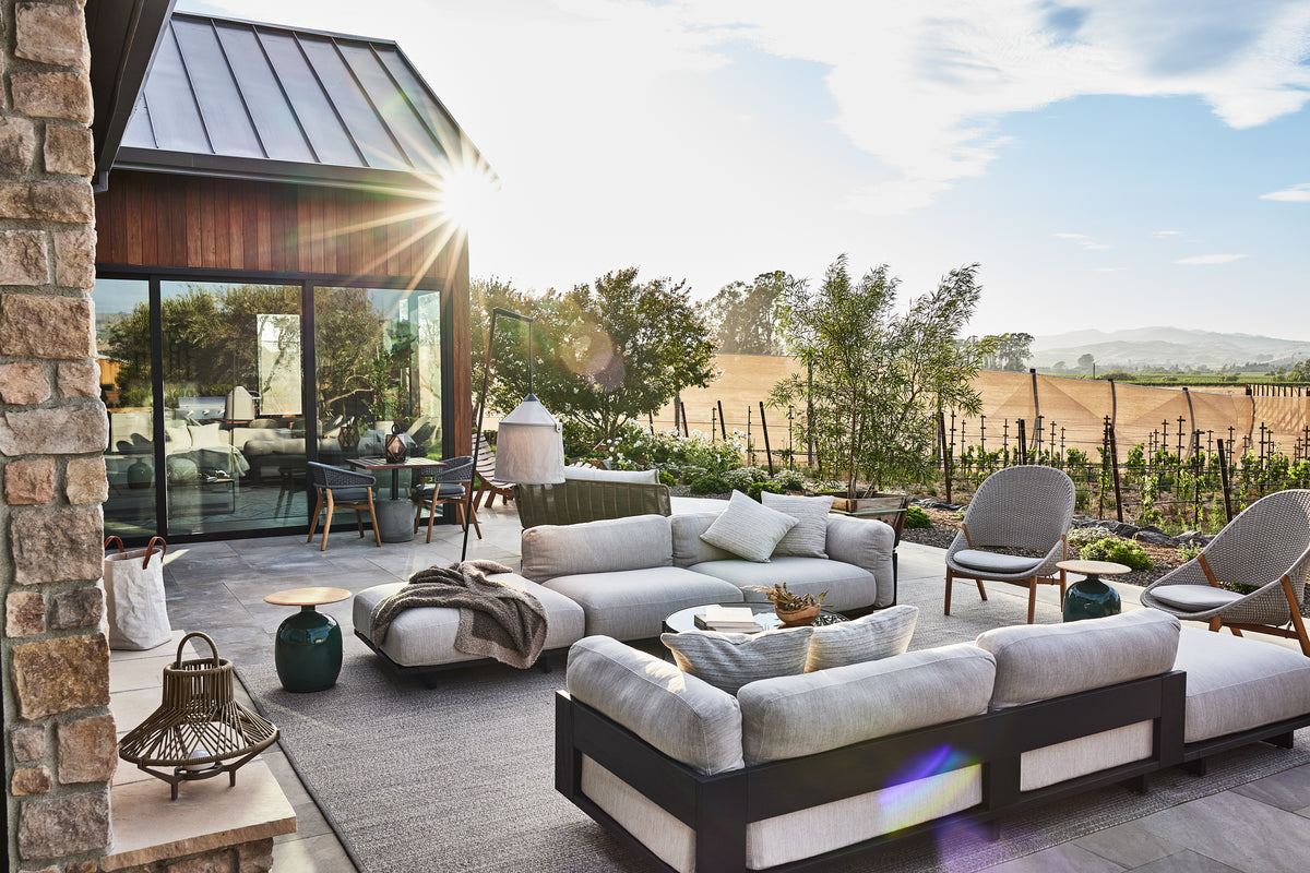 Sunlit outdoor patio with modern sofas and chairs overlooking vineyard rows and rolling hills