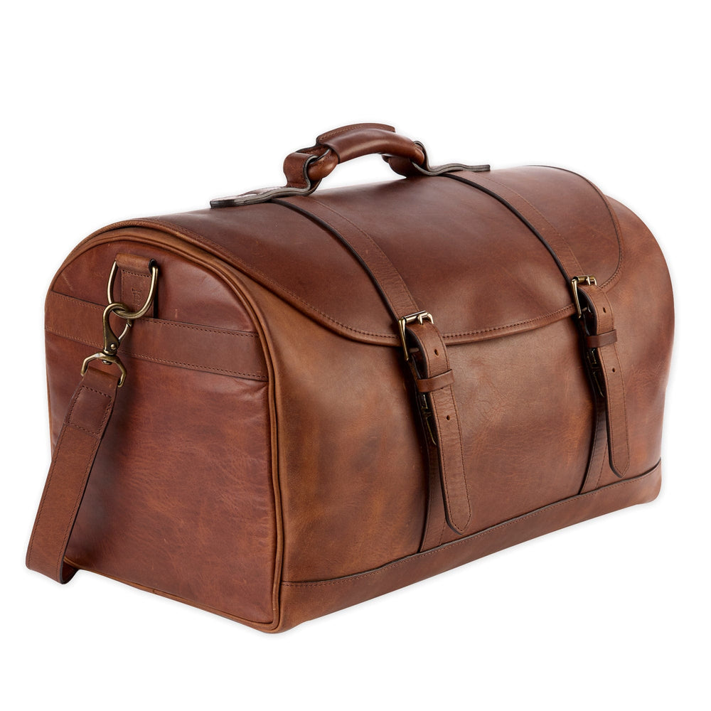 Three-quarter view of leather weekender duffel bag showing oak full-grain leather, brass hardware, roped handle and shoulder strap on white background