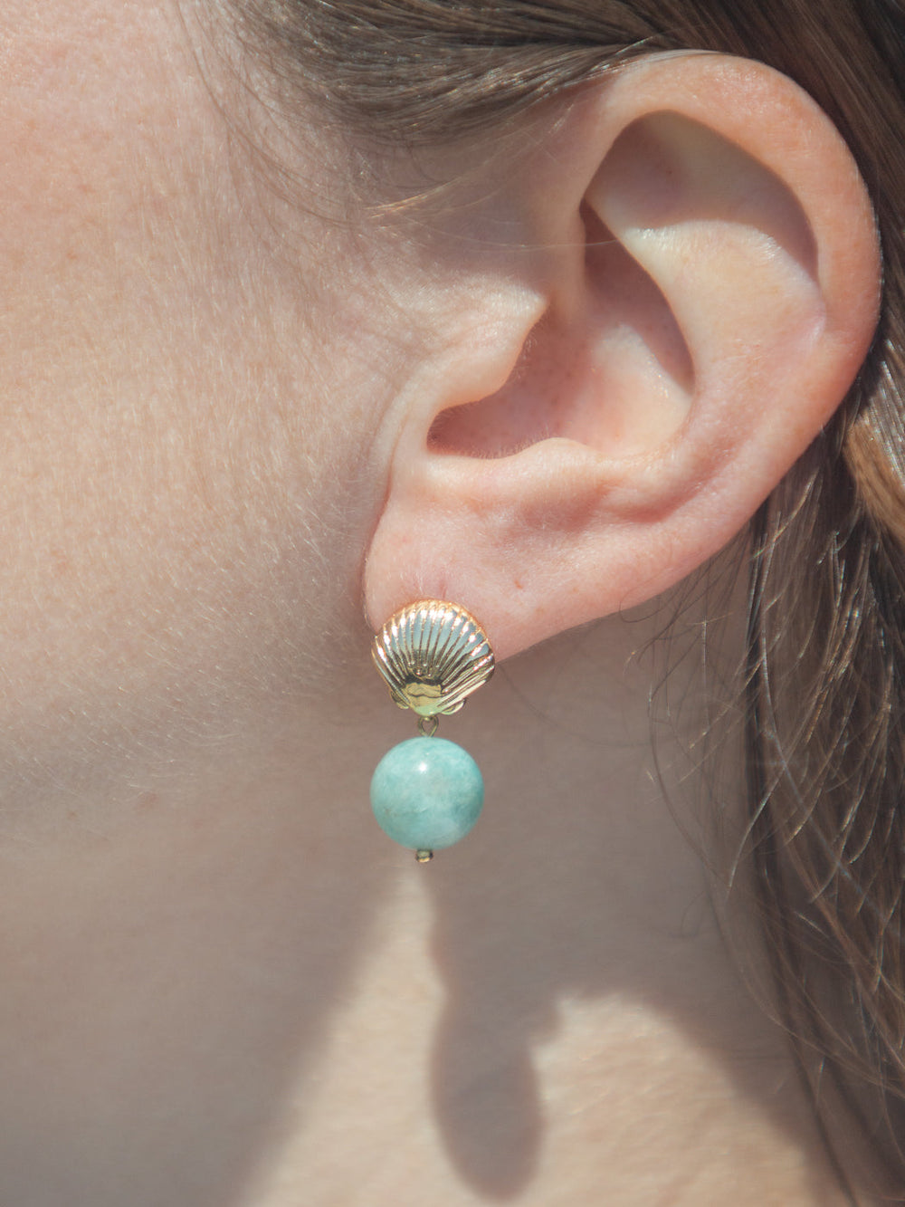 Close-up of Tori Earrings worn on ear showcasing gold-plated shell stud and dangling blue-green amazonite bead