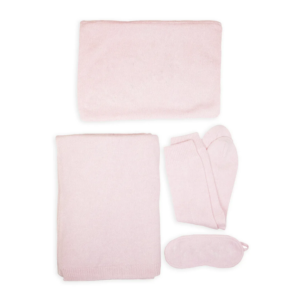 Top-down view of cashmere travel set with folded blanket, travel pouch, socks, and eye mask in pale pink on white background