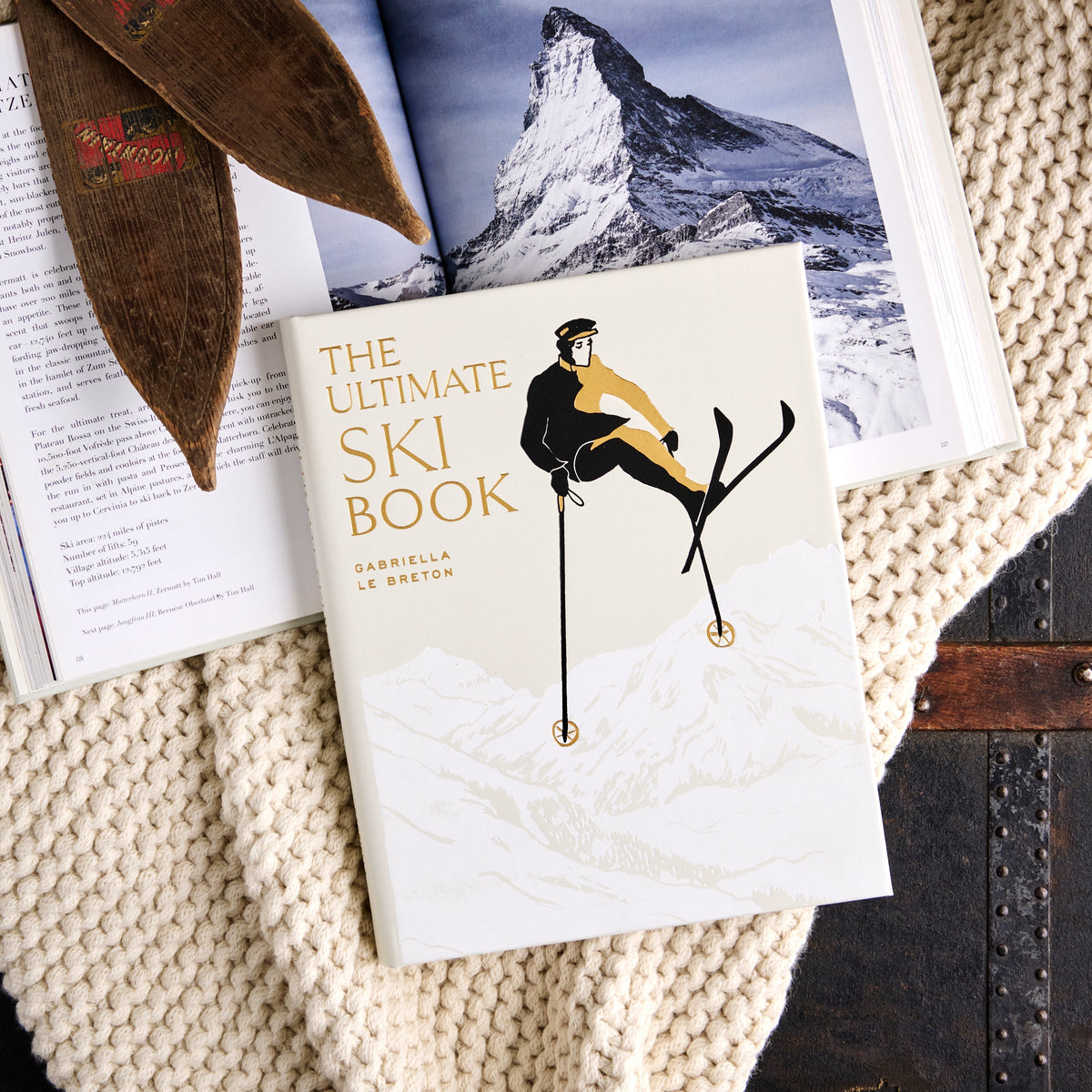 Overhead view of The Ultimate Ski Book showcasing its bonded leather cover and skier design with open alpine pages on a knit blanket