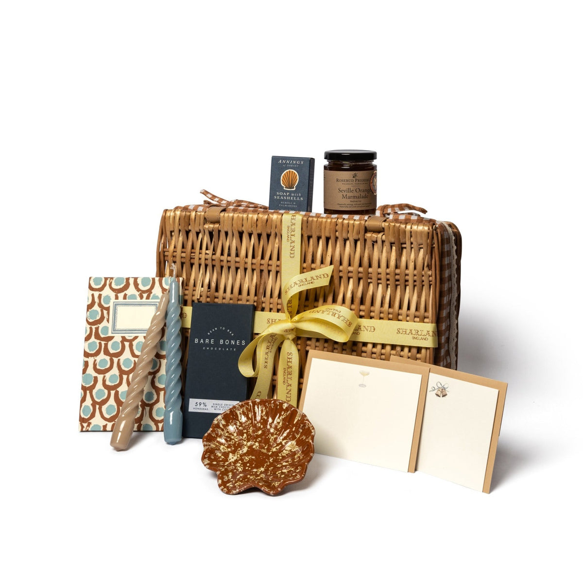 Front of The Chic Hamper wicker basket with yellow ribbon, scalloped dish, twisted candles, chocolate, jam and stationery