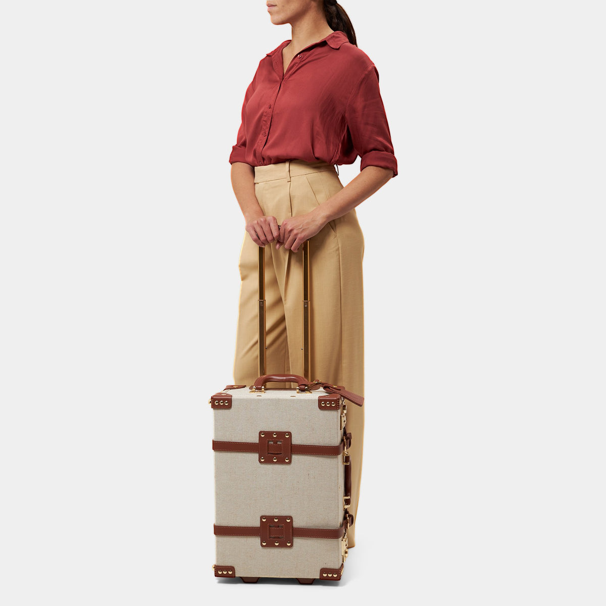 Front view of The Editor Carryon showcasing brown leather straps and extendable trolley handle with a light gray background