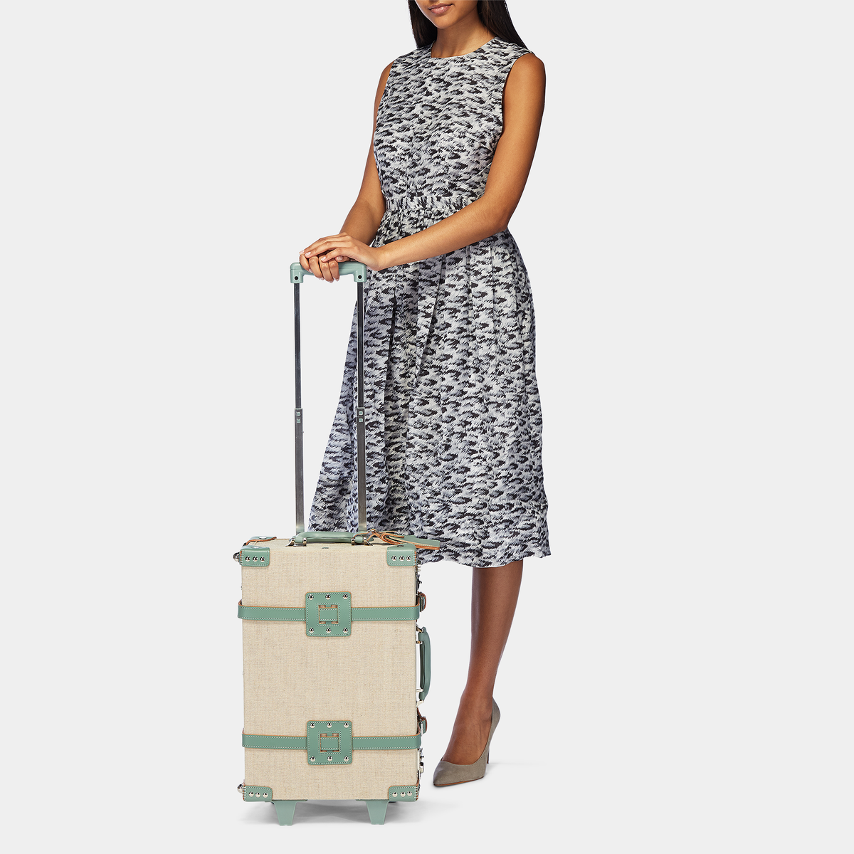 Front view of The Editor Carryon showing ivory body, sea green leather straps, and extended trolley handle on light gray background