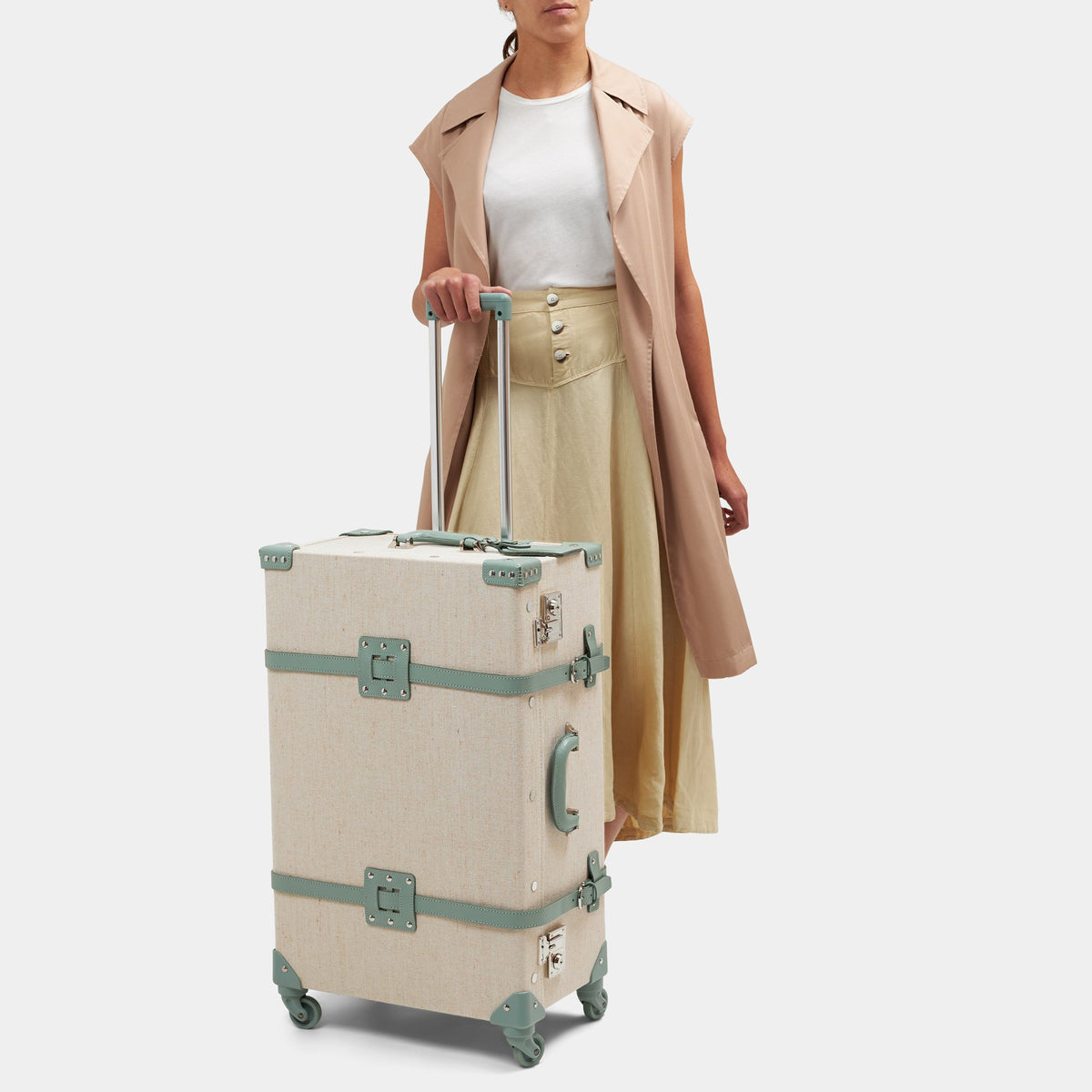 Three quarter view of The Editor Check In Spinner with ivory body, sea green leather straps, and extended trolley handle