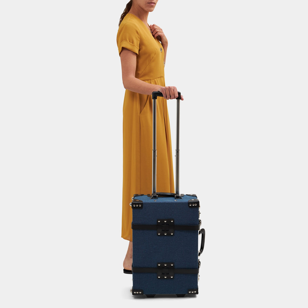 Front view of The Editor in Navy Carryon showcasing black leather straps and extendable trolley handle with a model on a light gray background