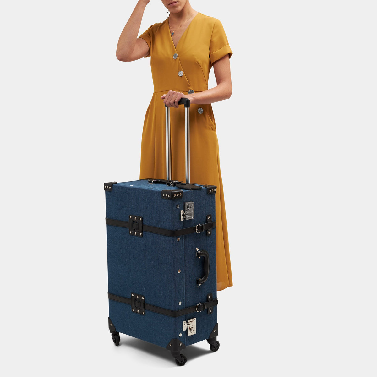 Front view of The Editor Check In Spinner showcasing navy linen, black leather straps, and extended trolley handle with model