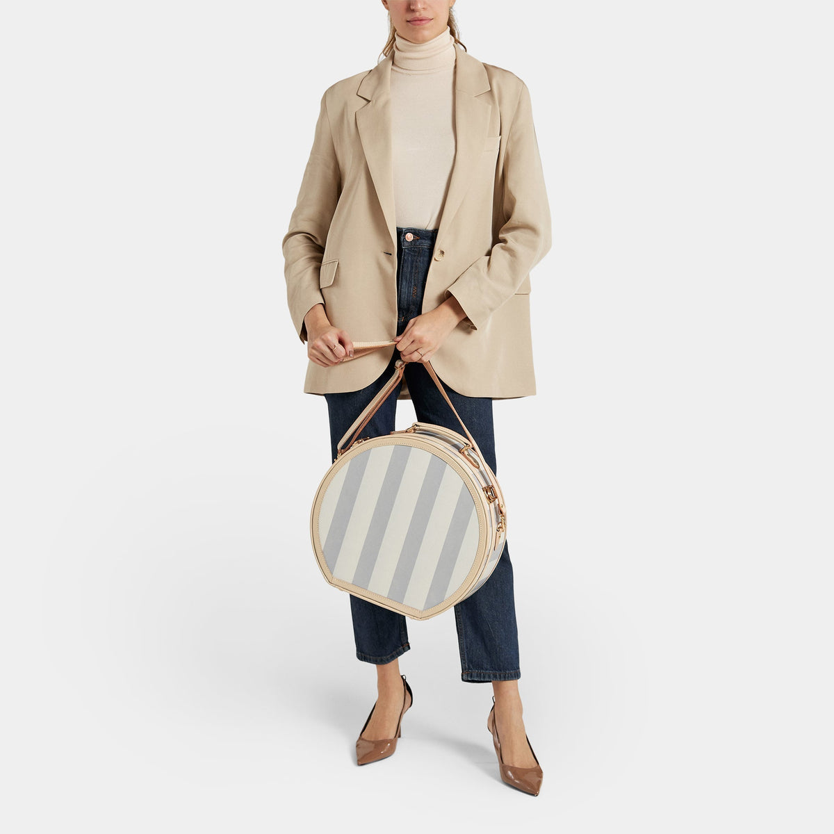 Front view of The Illustrator large blue hatbox with tan leather handles and gold hardware, held by model on white background