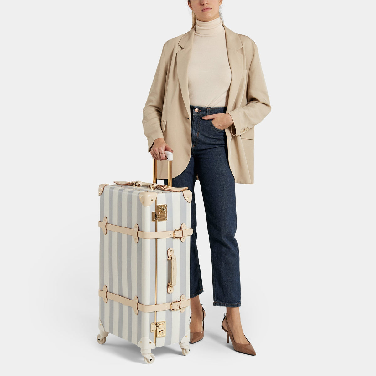 Front view of The Illustrator blue-check check-in spinner suitcase with tan leather trim and gold hardware on white