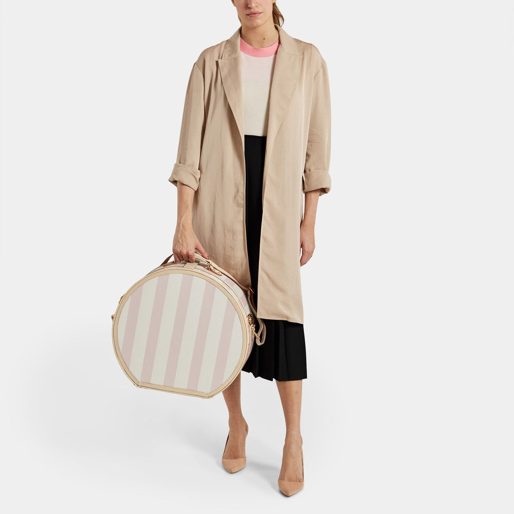 Model holding The Illustrator Deluxe pink hatbox with pink-and-cream stripes and tan leather trim on white background
