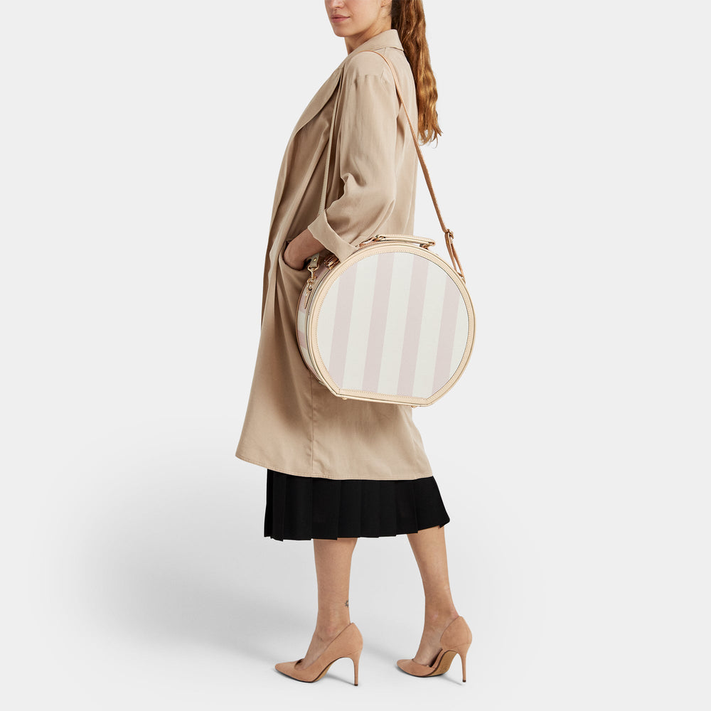 Side view of The Illustrator large pink hatbox with pink-and-white stripes, tan leather trim, shoulder strap on a model