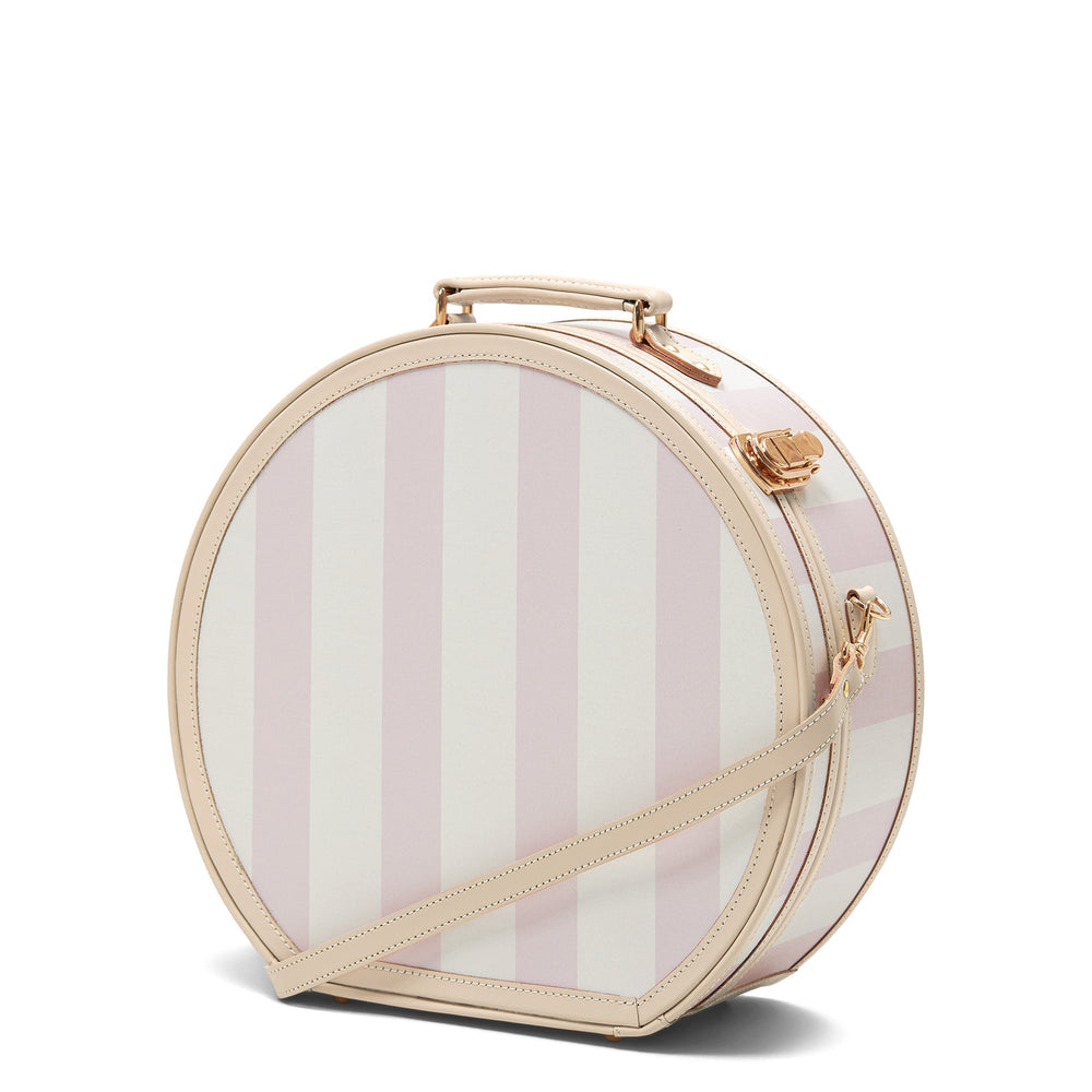 Three-quarter view of The Illustrator large pink striped hatbox with beige leather trim, detachable strap and gold hardware