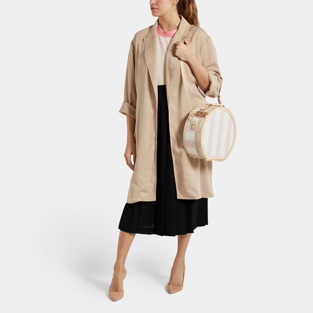 Three-quarter view of The Illustrator small pink hatbox on a model showing detachable shoulder strap and gold hardware