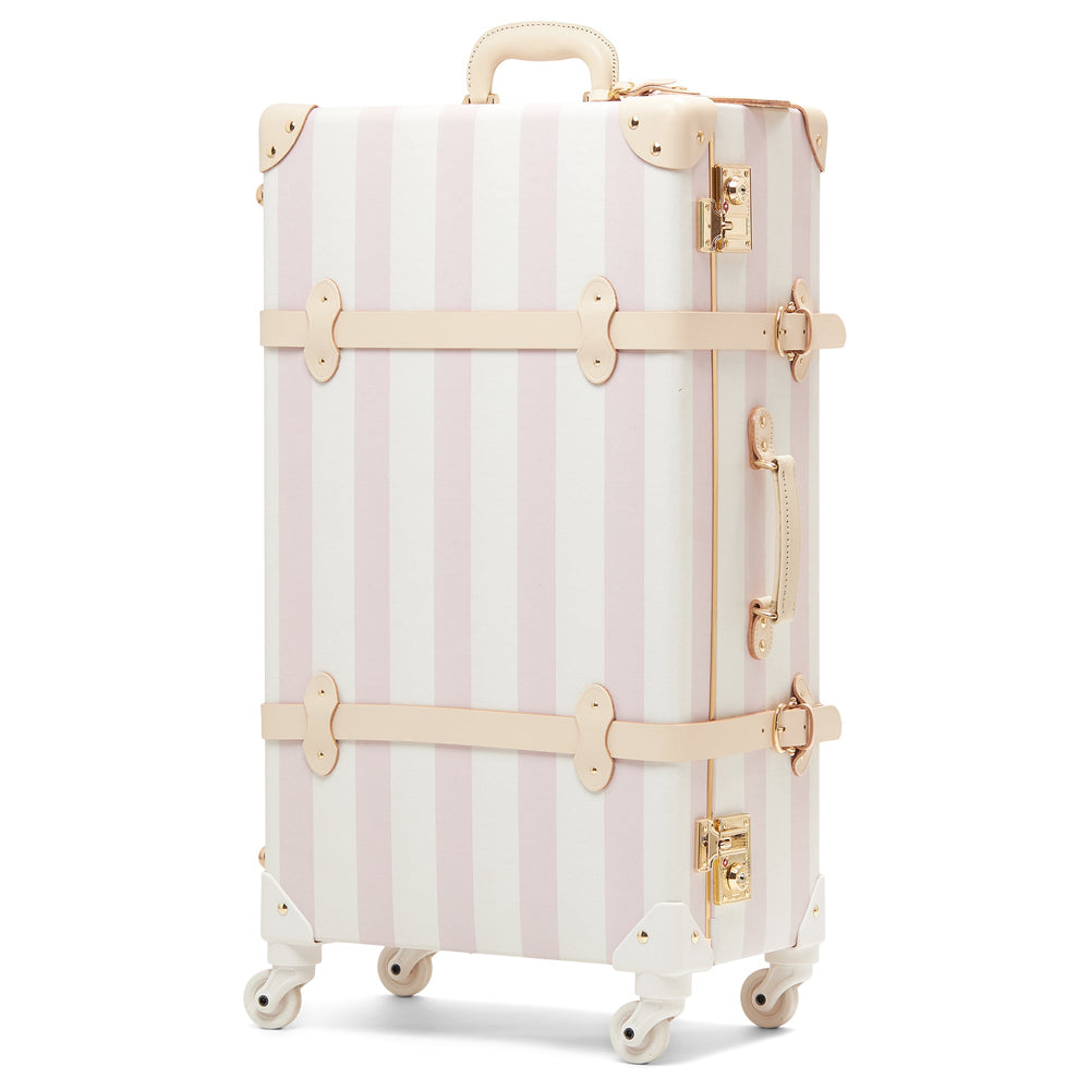 Angled view of The Illustrator Spinner in Pink Check with pink-and-white stripes, leather trim, gold hardware, four wheels on white background