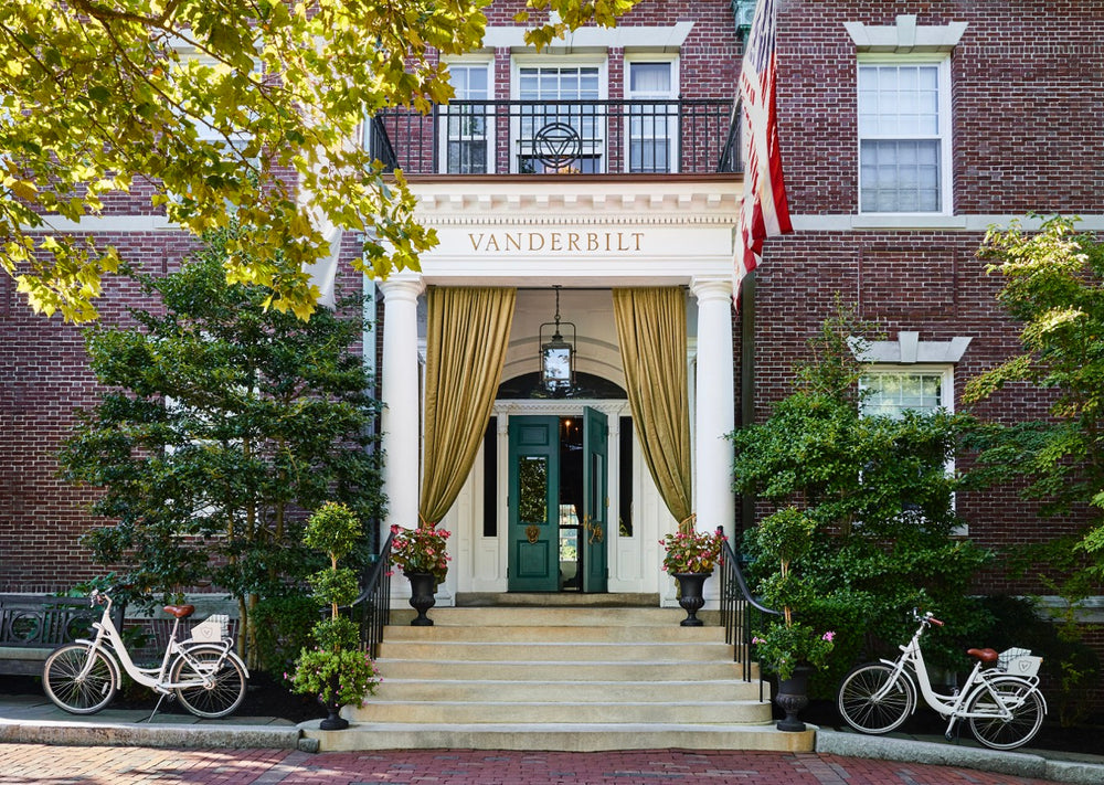 Front entrance of The Vanderbilt with columned portico, gold drapes, green doors, brick facade and two white bicycles