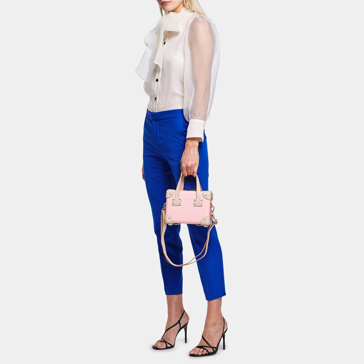 Front view of The Correspondent Pink Mini showcasing pink exterior, gold hardware, and tan straps with a model on gray background