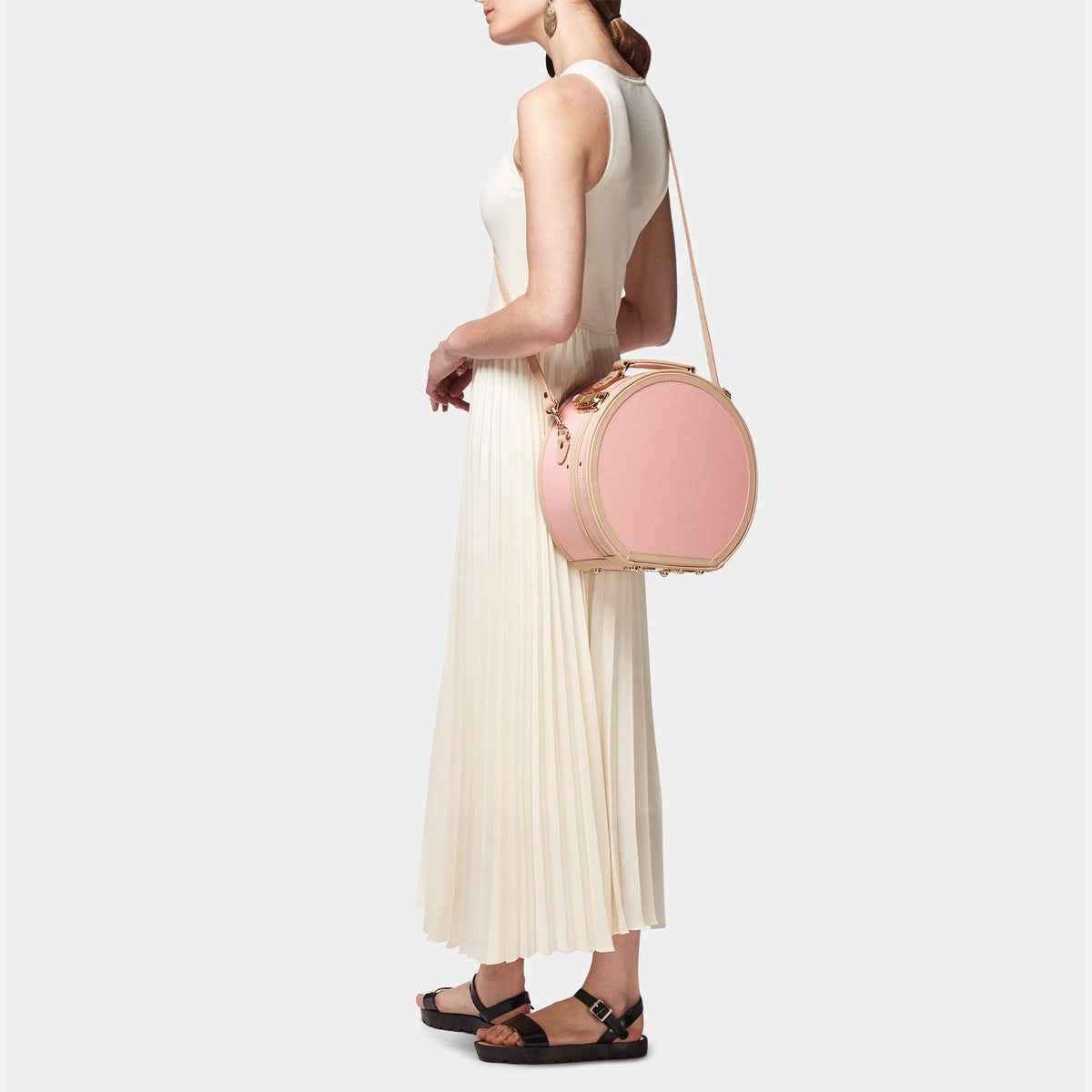 Side view of The Correspondent Pink Small Hatbox showcasing gold hardware and detachable shoulder strap on a model
