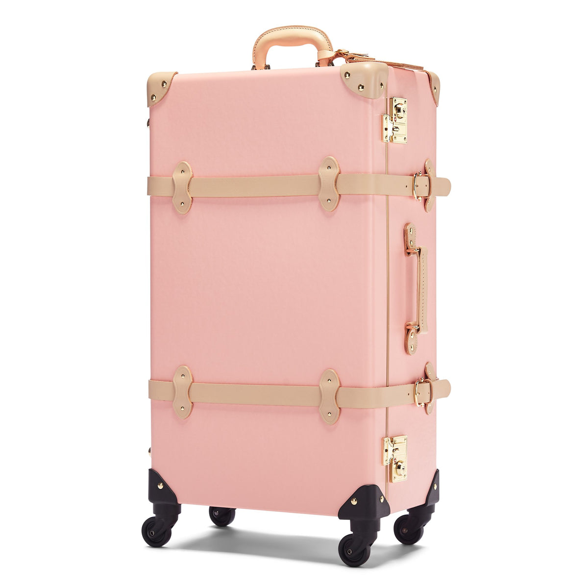 Front three-quarter view of The Correspondent Spinner showcasing pink fibreboard, leather straps, gold hardware, and four wheels on white background