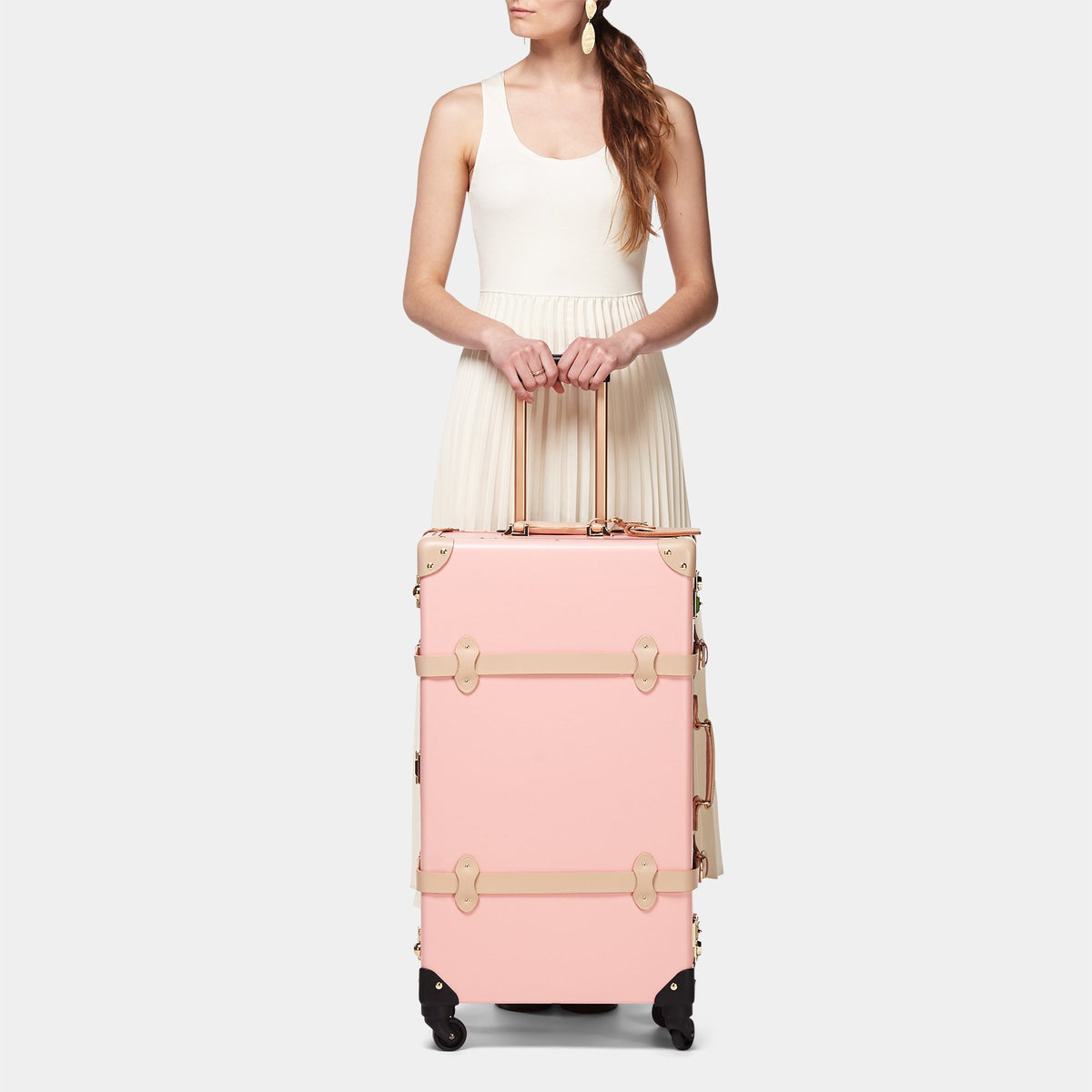 Front view of The Correspondent Pink Check In Spinner showcasing tan leather straps and gold hardware with a model on a light gray background
