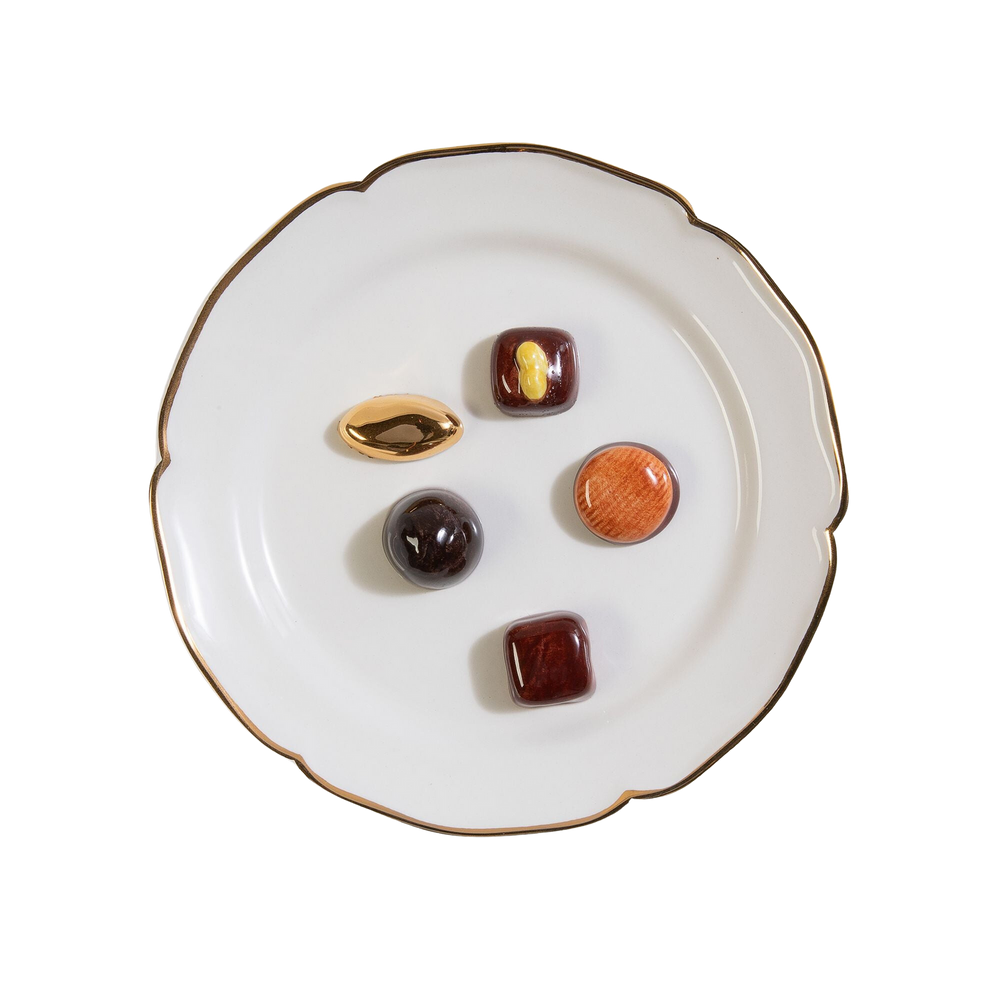 Top-down view of Trompe L’oeil Chocolat decorative plate showcasing scalloped gold-leaf rim and five hand-painted trompe l’oeil chocolate motifs on white background
