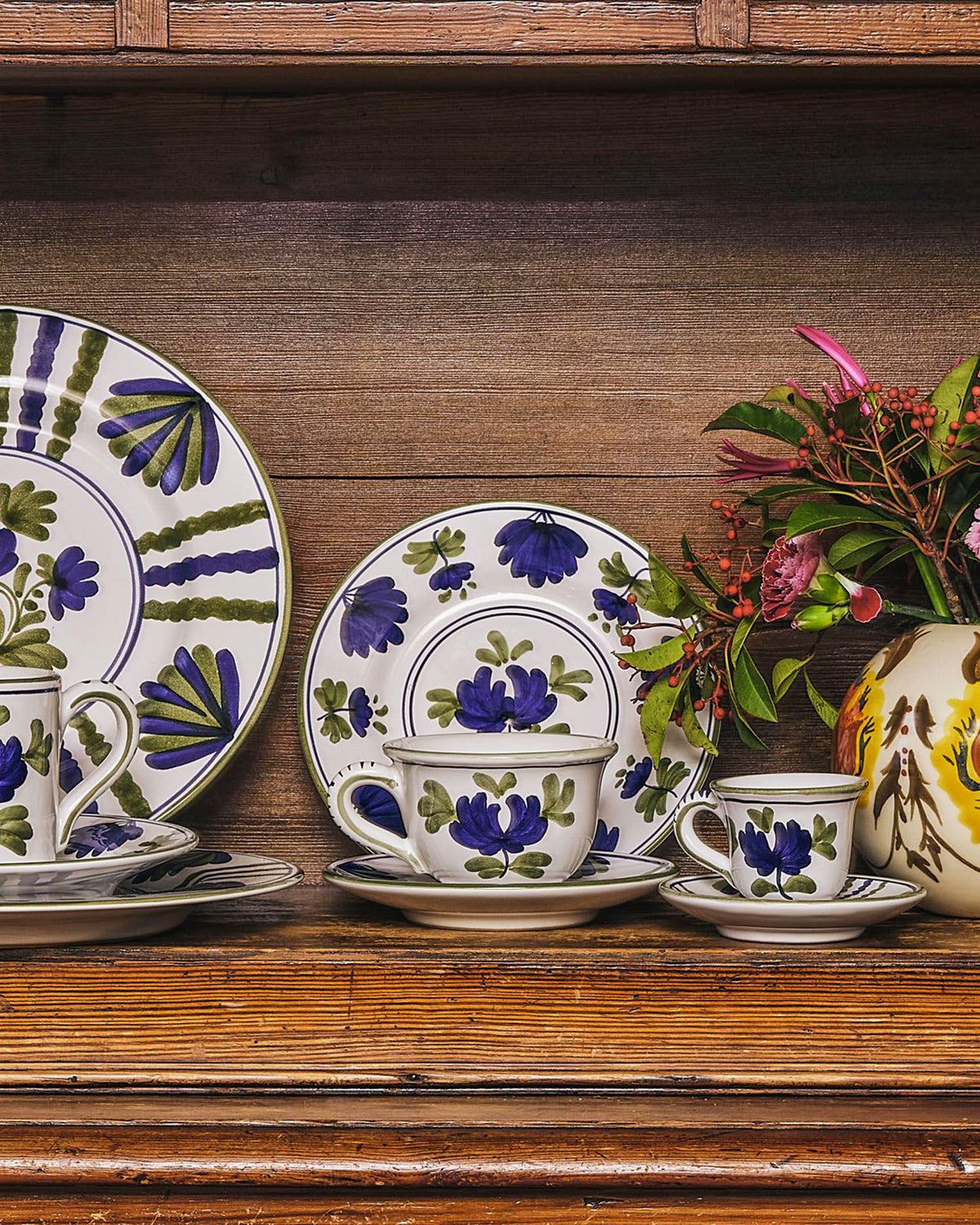 Front view of Blossom Teacup and Saucer in Blue showcasing hand painted blue and green floral motifs with a wooden tabletop background