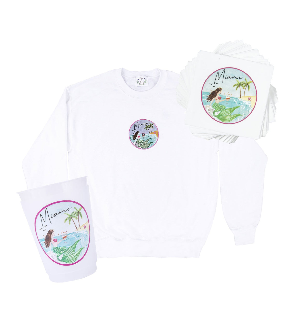 Front view of white crewneck sweatshirt, stack of napkins, and cup showcasing round Miami mermaid crest design on white background