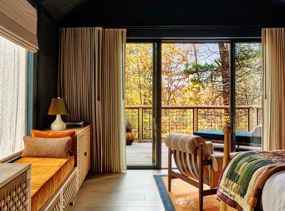 Cozy bedroom interior with sliding glass doors opening to a wood deck and autumn woods, orange velvet window bench and striped lounge chair