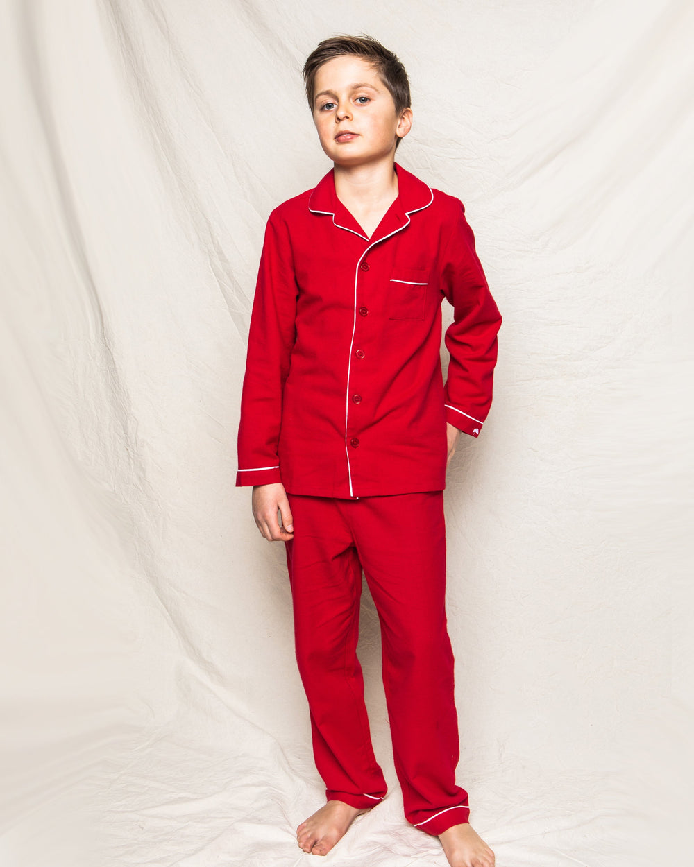 Front view of children’s classic red flannel pajama set showcasing white contrast piping and button-front top on a neutral fabric backdrop