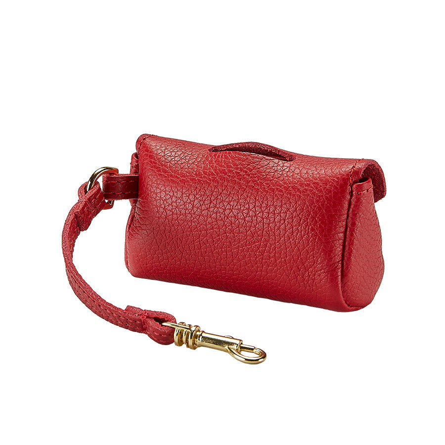 Three-quarter view of red pebble-grain leather pet waste bag holder showcasing antique brass hook clip on white background
