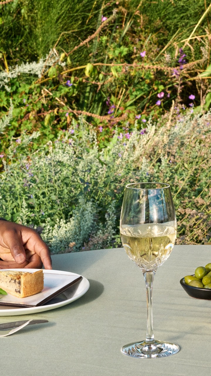 Waterford Lismore Essence wine glass filled with white wine on a table with a plate and bowl of olives in a garden