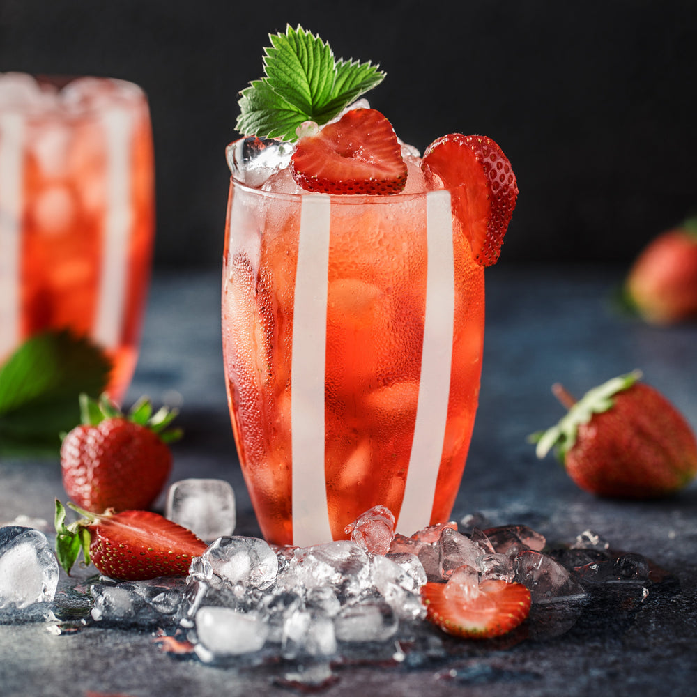Front view of Gessato Beverage glass showing vertical white stripes and a strawberry cocktail with ice on a dark background