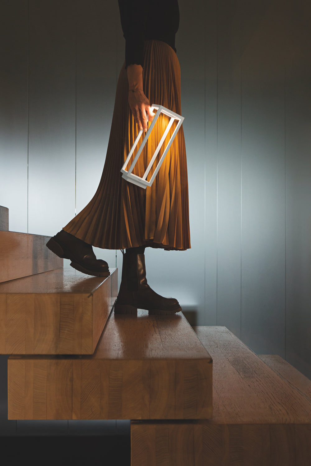 Person holding lit white Home Lamp while descending wooden stairs