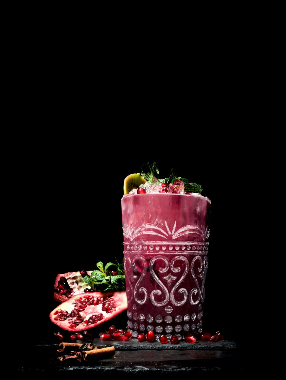 Front view of Provenzale Tumbler Rock showcasing embossed scroll pattern and beaded base, filled with pomegranate cocktail and mint on black background