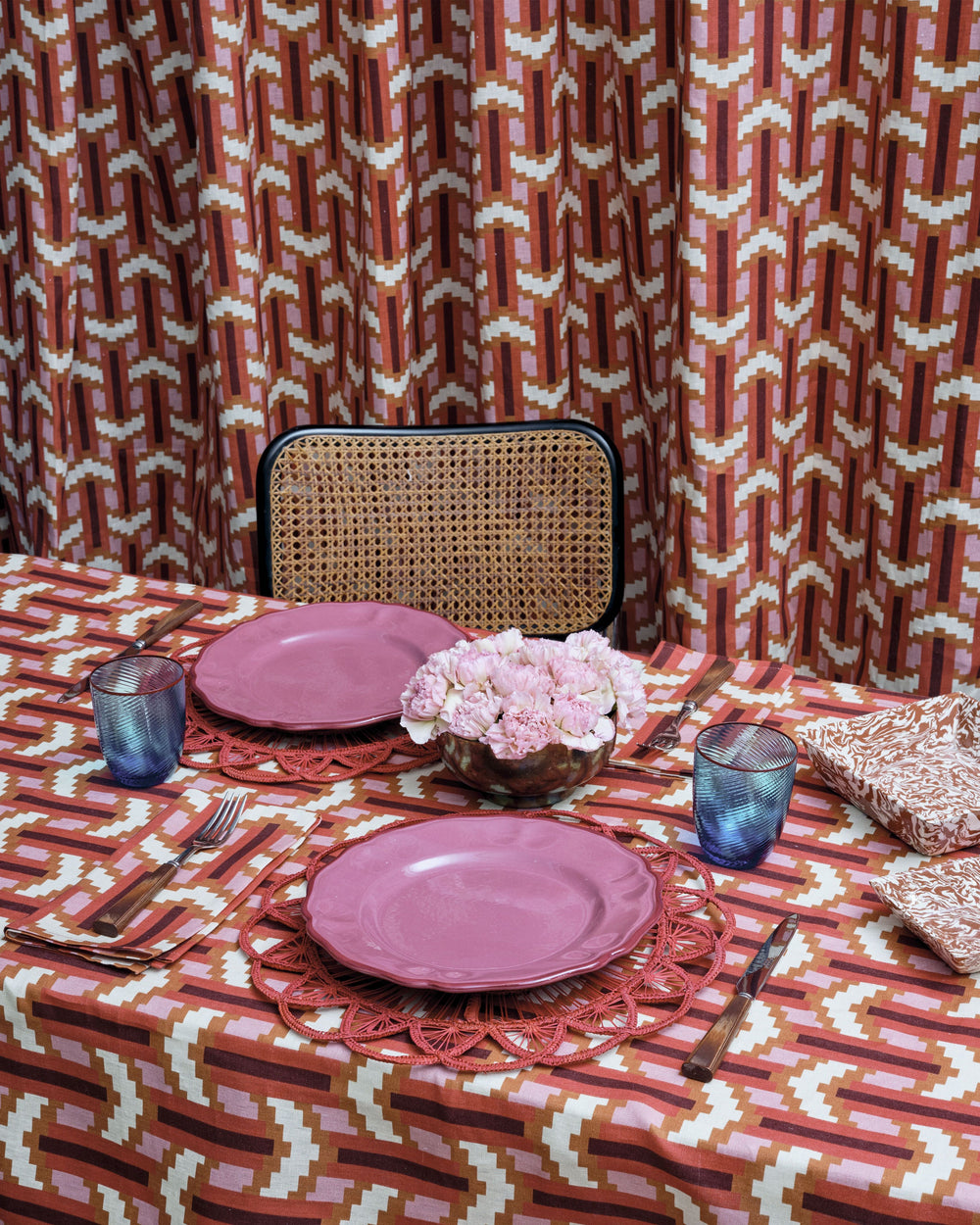 Overhead view of Britwell dinner plate in blush pink on a red woven placemat with geometric rust and pink tablecloth