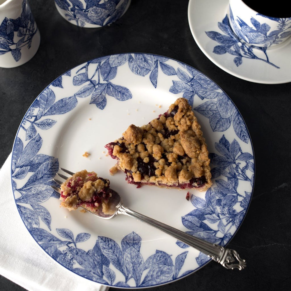 Top view of Arbor blue and white salad plate with leafy rim pattern, berry crumble slice and fork on dark surface