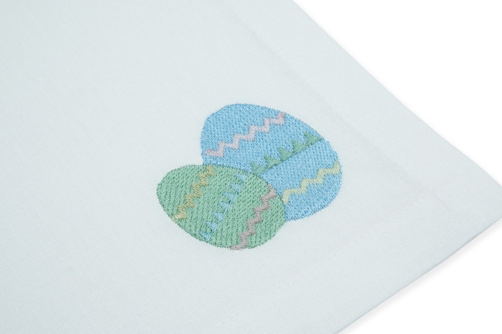 Close-up of white linen napkin showing embroidered blue and green Easter eggs