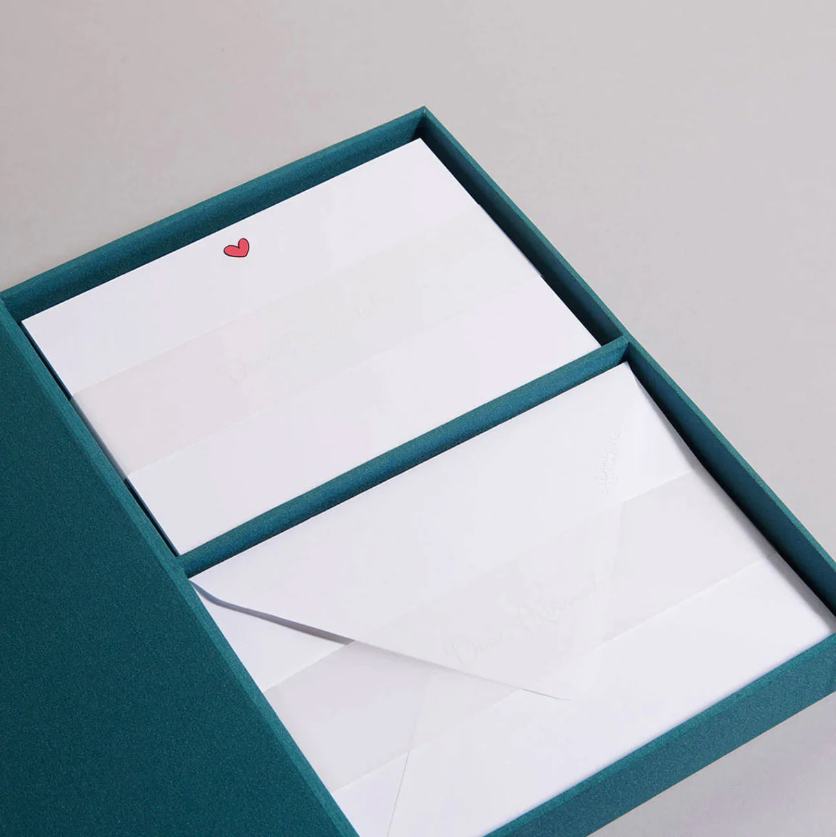 Angled view of Lovey Dovey notecards in teal keepsake box showing red heart on cards and white envelopes on gray background
