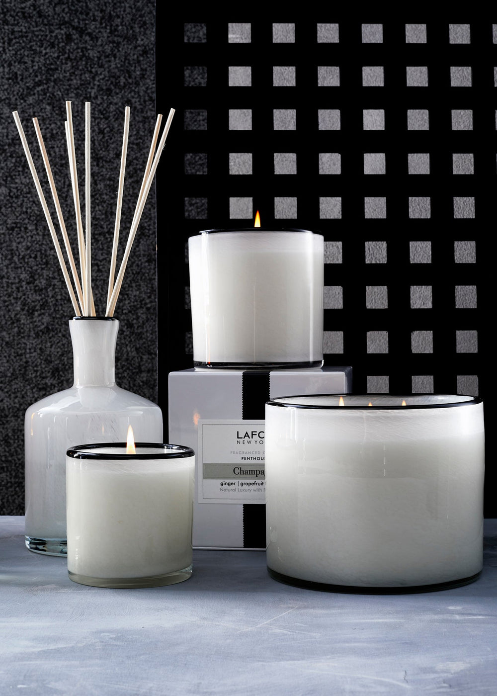 Front view of LAFCO Champagne candles and diffuser showcasing white frosted glass vessels with black rims and lit wicks
